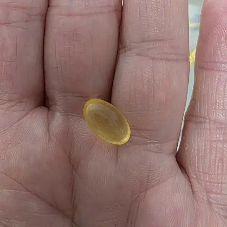 a hand holding a yellow hoki fish oil capsule pill